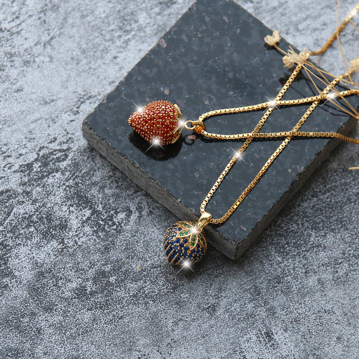 Set aus zwei Frucht-Halsketten: rote Erdbeere und blaue Variante mit Zirkonia – beide an 18K vergoldeter 925er Silberkette, perfekt als Geschenk.
