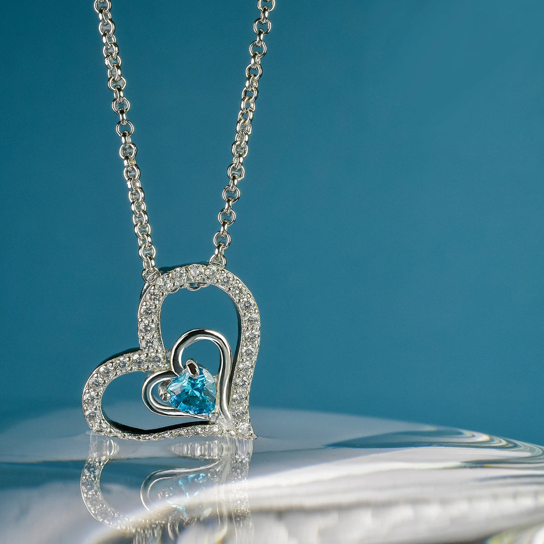 Feine Herz-Halskette Lovely Blue mit hellblauem Zirkonia – edles Schmuckfoto in Silber auf blauem Hintergrund, romantisches Accessoire.