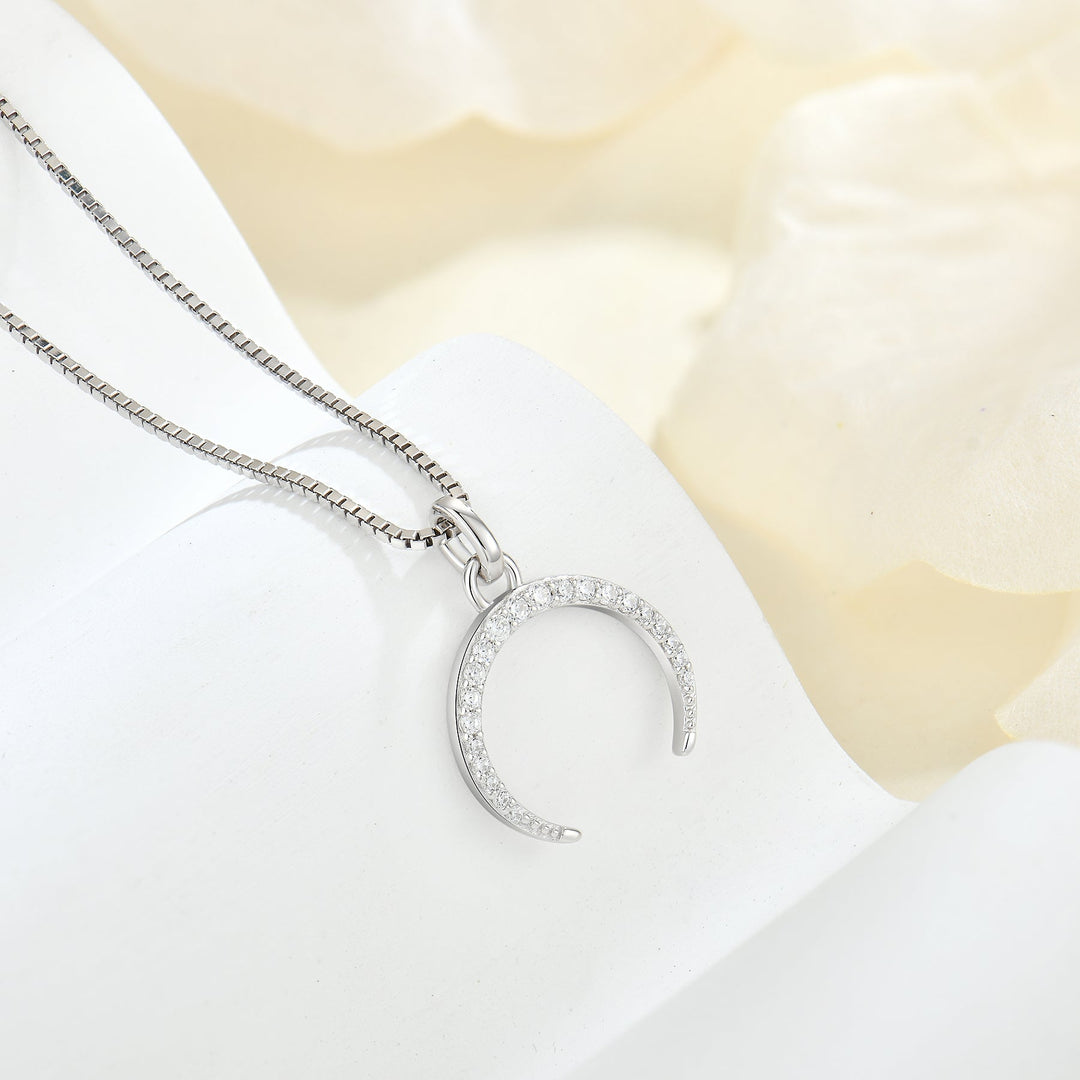 Halskette mit Halbmond aus Silber und Zirkonia auf hellem Stoff – femininer Schmuck im sanften Design
