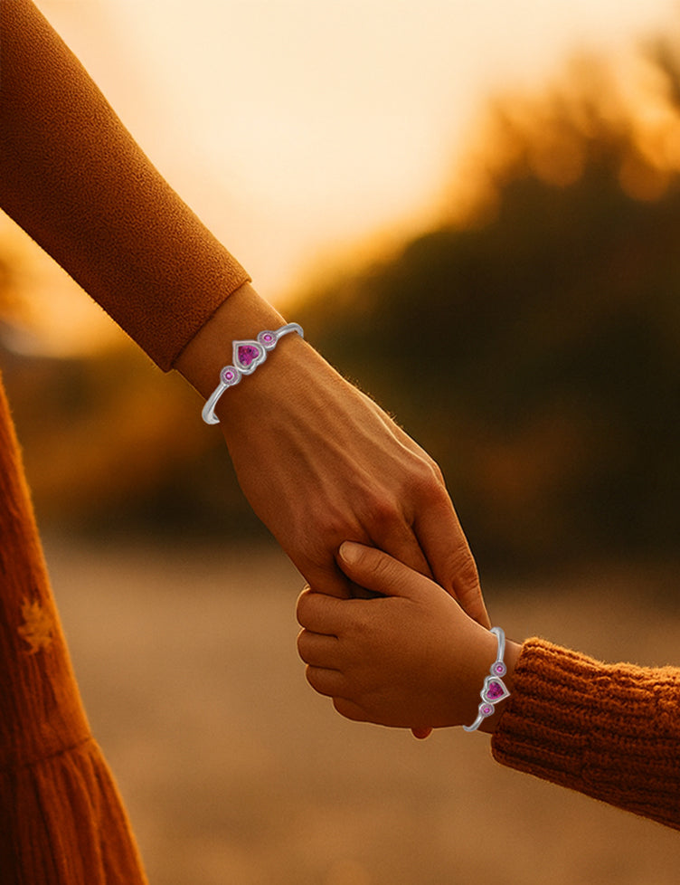 Mutter und Kind halten sich an den Händen und tragen passende Herzarmbänder bei warmem Licht eines herbstlichen Sonnenuntergangs.