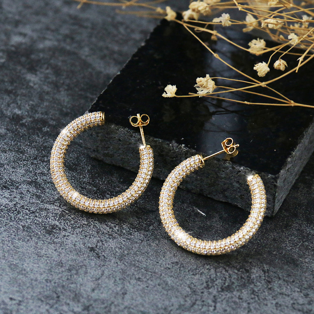 Glamouröse Creolen Bonny Gold aus 925 Sterling Silber – luxuriöse vergoldete Damen Hoop-Ohrringe mit funkelnden Zirkonia, präsentiert auf schwarzer Steinplatte. Eleganter Statement-Schmuck für Abendmode, Events und festliche Outfits.